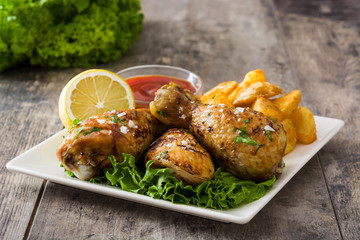 Roast chicken drumsticks and chips on wooden table

