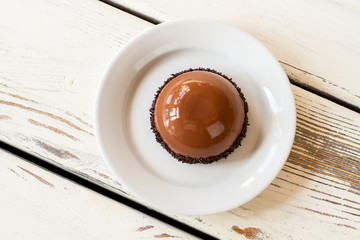 Small glazed cake on plate. Top view of brown dessert. Mirror glaze and chocolate mousse. Freshly made dish in cafeteria.