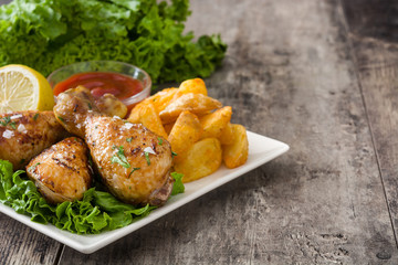 Roast chicken drumsticks and chips on wooden table

