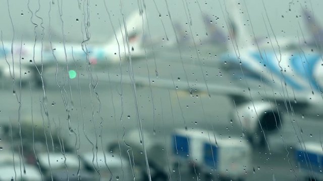 Raindrops on the window of airport terminal with blur airport outside. Slow motion.