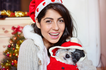Women with braces  on teeth hugging her  small poodle dog with red  christmas hats 