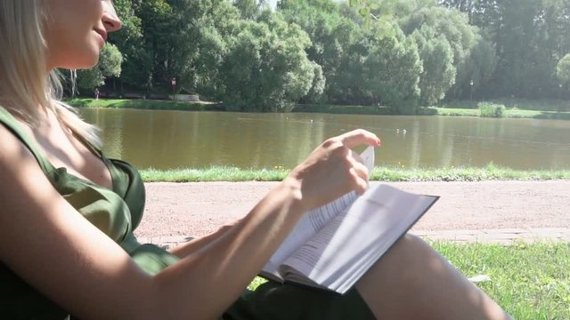 Pregnant blonde girl sits under a tree in a park and reading a book