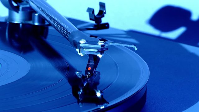Gentle slide shot of a tonearm on a long playing record (LP), with a distinct blue cast (front view). 