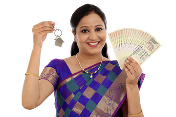 Happy young traditional woman holding Indian currency and house
