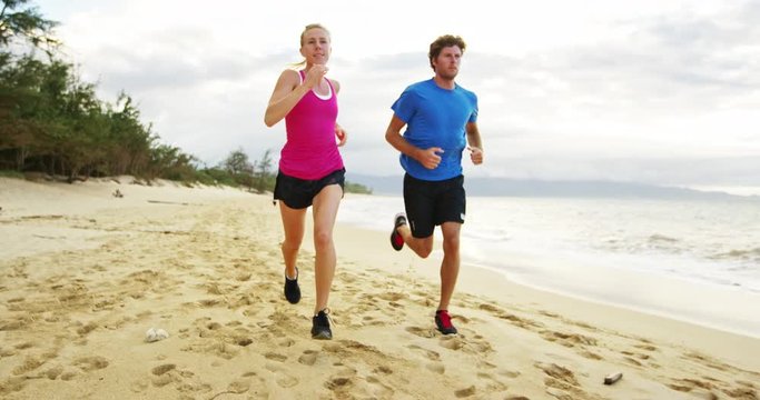 Athletic couple jogging together on the beach at sunset