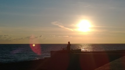 Naklejka na ściany i meble Мужчина в шляпе на закате на берегу смотрит вдаль моря