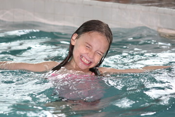 Girl child frolicking in the shallow end of a swimming pool. 

