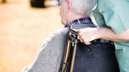 Elder people with wheelchair assisted by nurse outdoor