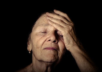 Portrait of elderly woman. Closes eyes with hands. Toned