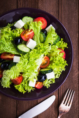 Greek salad (lettuce, tomatoes, feta cheese, cucumbers, black olives) on dark wooden background top view. Healthy food.