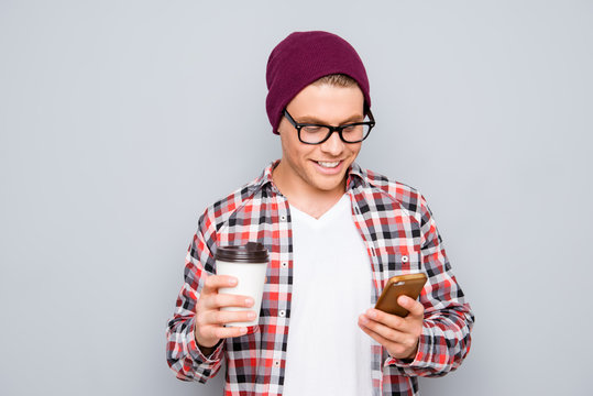 Young hipster in glasses with cup of coffee writing sms on smart