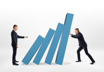 Fototapeta premium Rival businessman pushing the blocks of graph that another holding back from falling