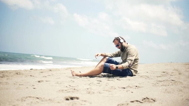 Sad, unhappy man listen to music on cellphone sitting on beach near sea
