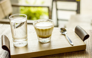 Cappuccino coffee cup with glass of water serving on wooden tray on coffee table