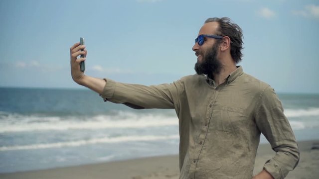 Happy man taking selfie photo with cellphone standing on beach near sea
