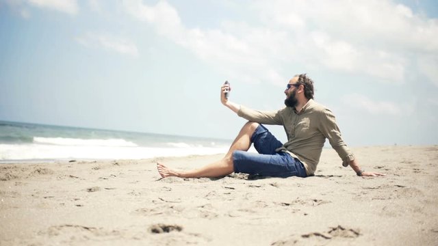 Happy man taking selfie photo with cellphone standing on beach near sea
