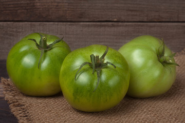 three green unripe tomato on the wooden background with burlap