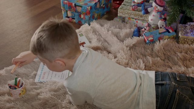 Little boy lying under christmas tree and write a letter to santa claus
