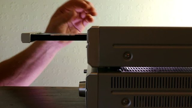 Backlit shot of hands placing a disc into a CD player. 