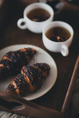 Two cups of tea with cinnamon sticks and anise stars and two croissants on a plate in a cozy room