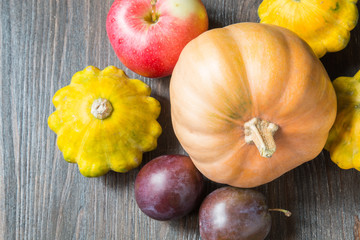 Pumpkin with zucchini, apples and plums on a dark wooden background