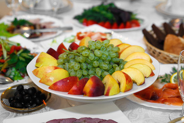 Fototapeta na wymiar Fruit sliced on white plate. The serving of the dinner table apples and grapes. Useful vitamin food for dessert.