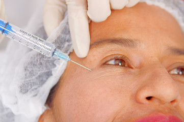 Closeup womans face receiving botox injections with syringe, cosmetic surgery concept, as seen from above