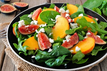 Autumn salad of arugula, spinach figs and goat cheese in a black plate on a rustic wooden background