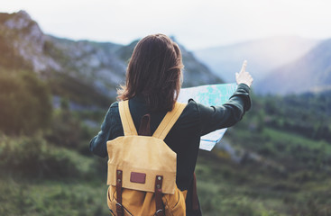 Hipster young girl with backpack enjoying sunset on peak of foggy mountain, looking a map and...