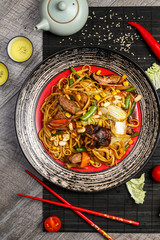 Traditional Japanese cuisine, noodles with chicken and vegetables on a black plate with chopsticks