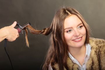 Stylist curling hair for young woman.