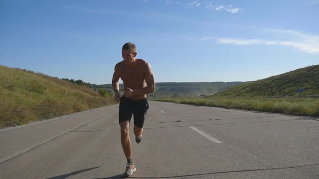 Sprinting runner man jogging at highway. Male sport athlete training outdoor at summer. Young strong muscular guy exercising on rural road during workout. Active healthy lifestyle outside. Slow motion