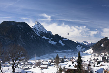 Landscape of Gstaad in Switzerland, with snow in winter, with a with a hot-air balloon in the blue sky
