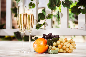 Autumn fruits and two glasses of white wine at the light background. Horizontal