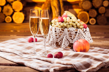 two glasses of white wine and juicy fruits in the wicker basket on checkered plaid at the wooden logs background