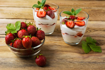 Ripe strawberries and layered cream cheese dessert on wooden bac