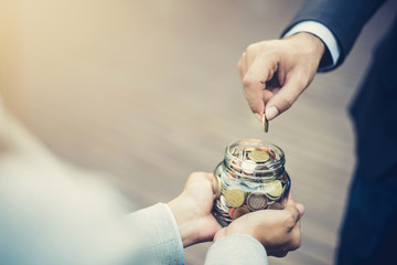 Businessman hand putting money (coin) in the glass jar held by a woman