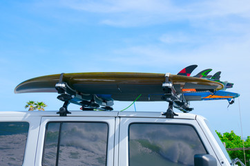 Surfboards on surf racks on a white truck with big waves reflections in the windows on a bright sunny day.