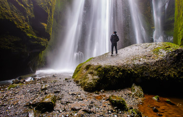 A man standing on a big rock enjoying the scene of waterfall, Iceland. Glyufrafoss waterfall in the gorge of the mountains. Tourist Attraction Iceland.  Beauty in nature.