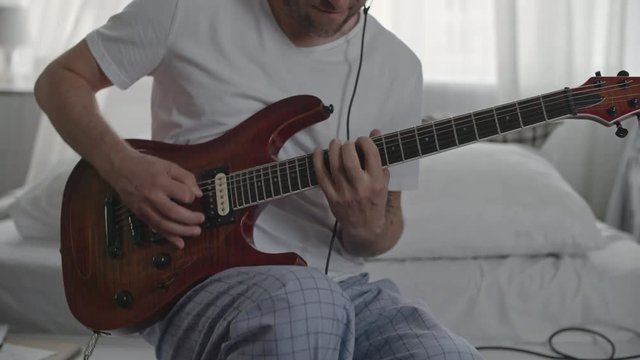 Tilt up of musician sitting at home with headphones and playing the guitar
