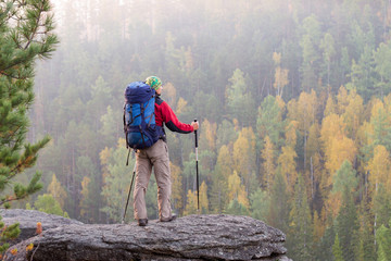 Man with backpack and trekking pole in bandana standing on a roc