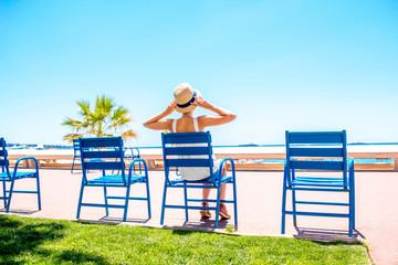 Woman sitting on the blue chairs of the promenade in Cannes city. This chairs are iconic symbol and...
