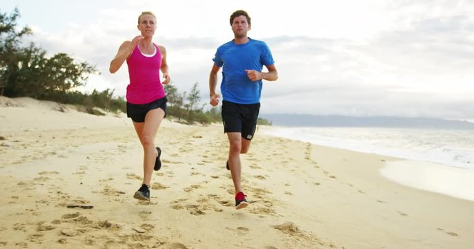 Athletic couple jogging together on the beach at sunset