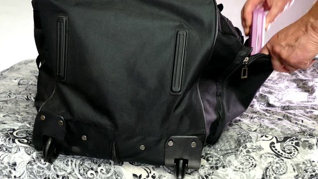 Hands add belongings to a side pocket of a soft travel case.
