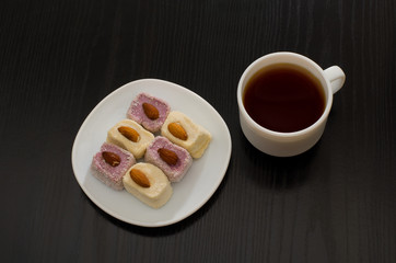 Top view of Turkish delight with almonds and cup of coffee, black table