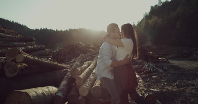 Happy young couple enjoying an intimate moment near logs in forest  , man gently strokes his partner's hair at sunset. Video in 4k
