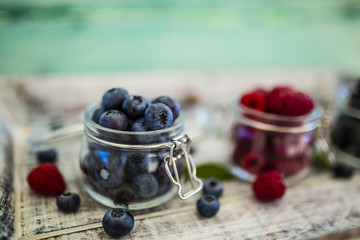 Tasty ripe and fresh forest fruits in glass jars on wooden background.