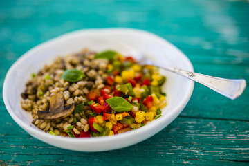 Barley groats with vegetables and herbs served on a plate on a wooden table. Vegetarian food. 