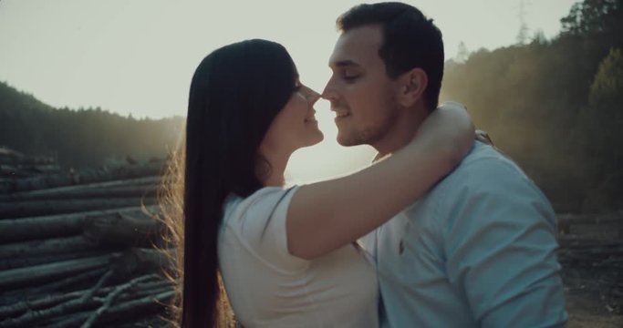 A young couple hug and kiss each other beside logs .