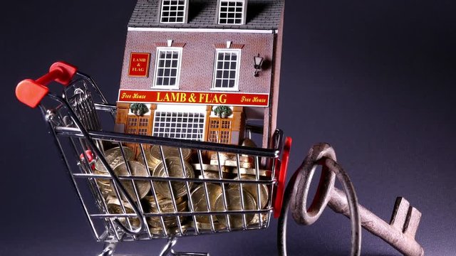 Slider shot of a model British pub (with fictitious name) in a shopping trolley, with pound coins and a large set of keys. Concept of buying or renting a business.